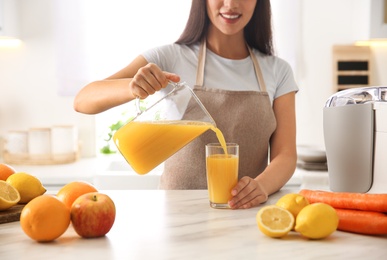 Photo of Young woman pouring tasty fresh juice into glass at table in kitchen, closeup