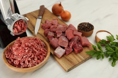 Photo of Electric meat grinder with beef and products on white marble table, above view