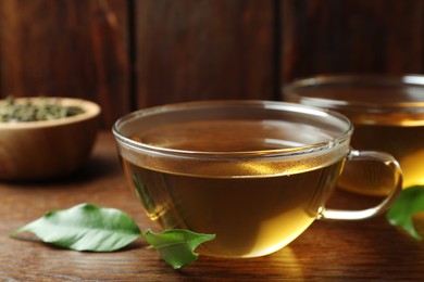 Photo of Fresh green tea in glass cup and leaves on wooden table, closeup