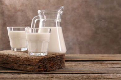 Photo of Jug and glasses of fresh milk on wooden table, space for text