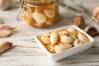 Preserved garlic in bowl on wooden table, closeup