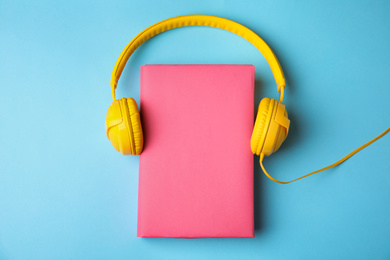 Book with blank cover and headphones on light blue background, flat lay