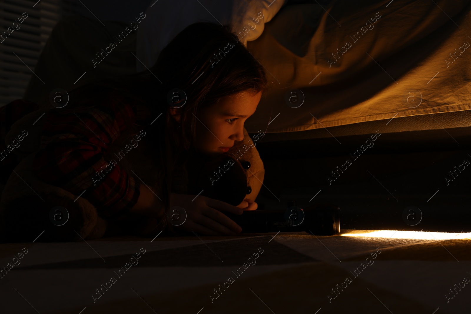 Photo of Little girl with flashlight looking for monster under bed at night