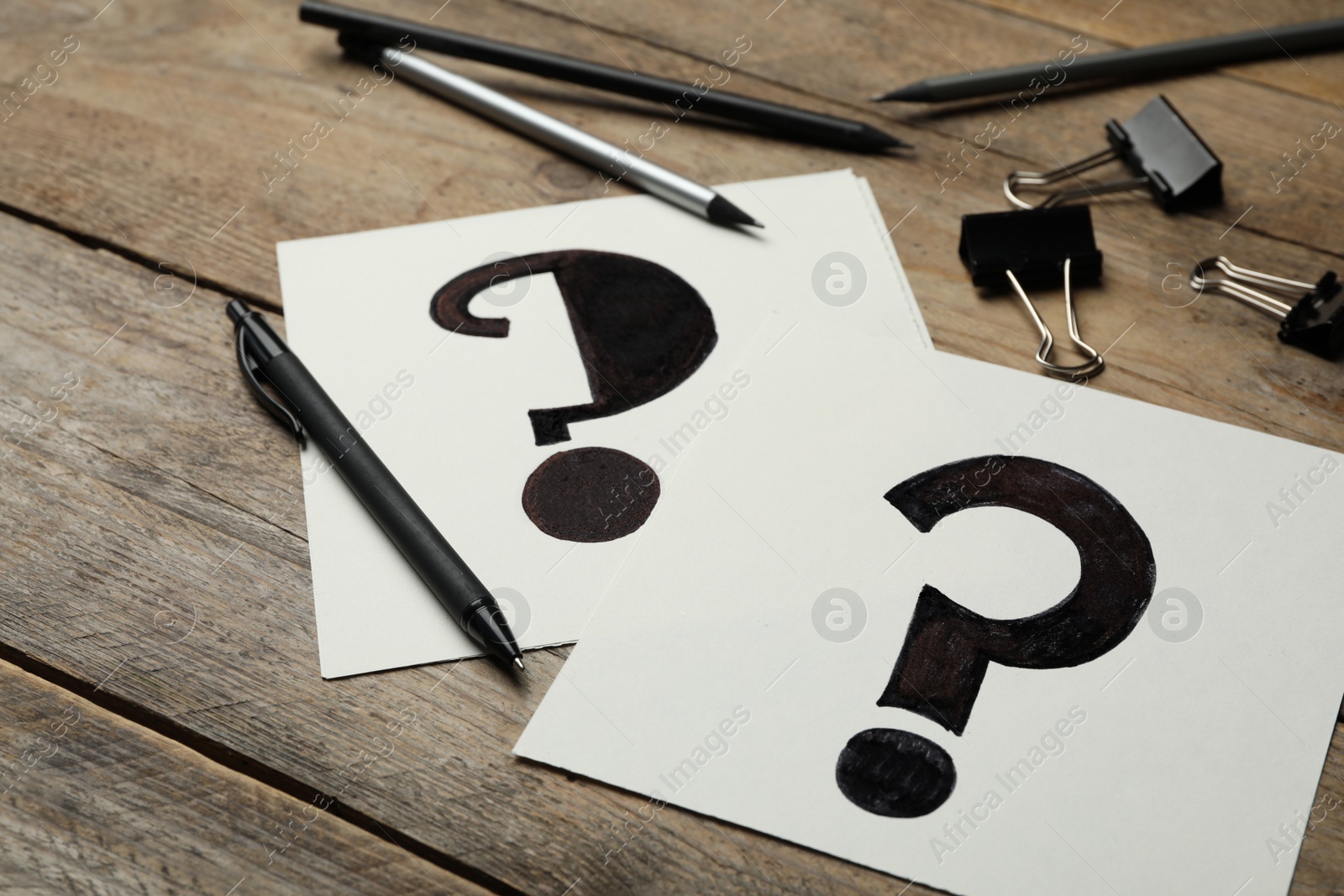 Photo of Notes with question marks and pen on wooden table, closeup