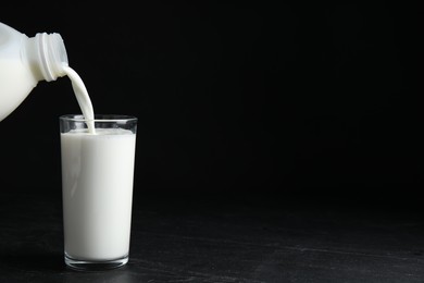 Photo of Pouring milk from gallon bottle into glass on black table. Space for text