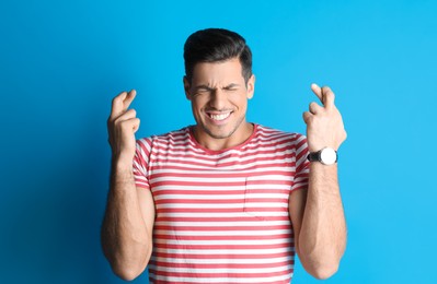 Photo of Man with crossed fingers on light blue background. Superstition concept