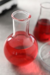 Laboratory analysis. Flasks with red liquid on light grey table, closeup