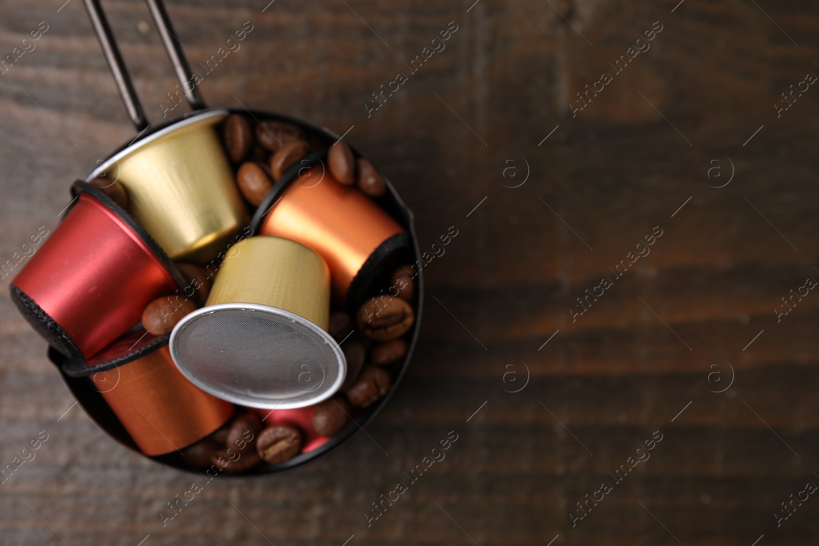 Photo of Saucepan with coffee capsules and beans on wooden table, top view. Space for text