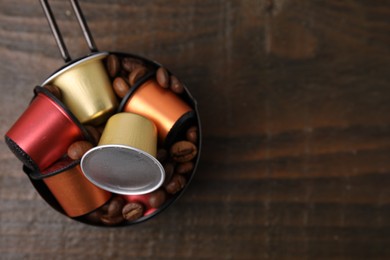 Saucepan with coffee capsules and beans on wooden table, top view. Space for text