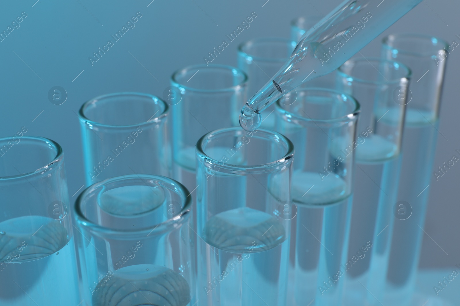 Photo of Laboratory analysis. Dripping liquid from pipette into glass test tube on light blue background, closeup