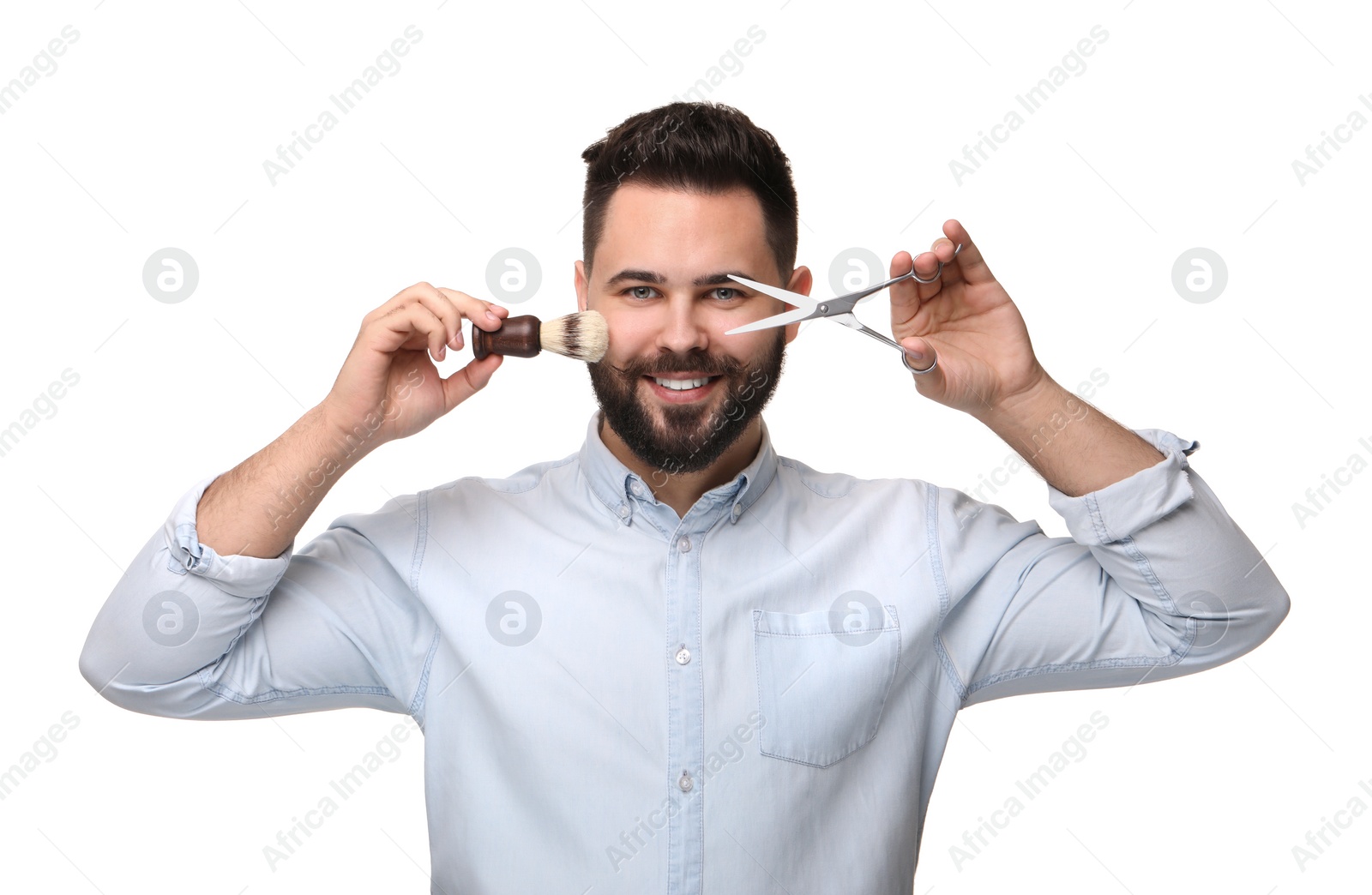 Photo of Handsome young man with mustache holding scissors and shaving brush on white background