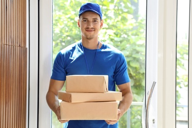 Happy young courier with pile of parcels in doorway