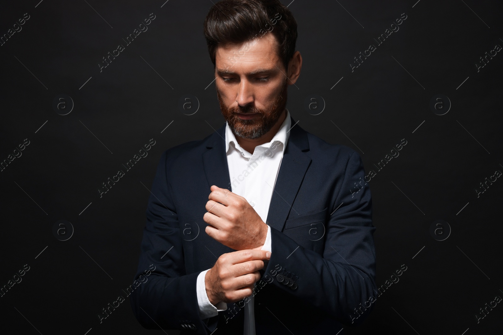 Photo of Handsome bearded man adjusting cufflinks on black background