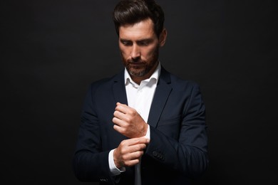 Photo of Handsome bearded man adjusting cufflinks on black background
