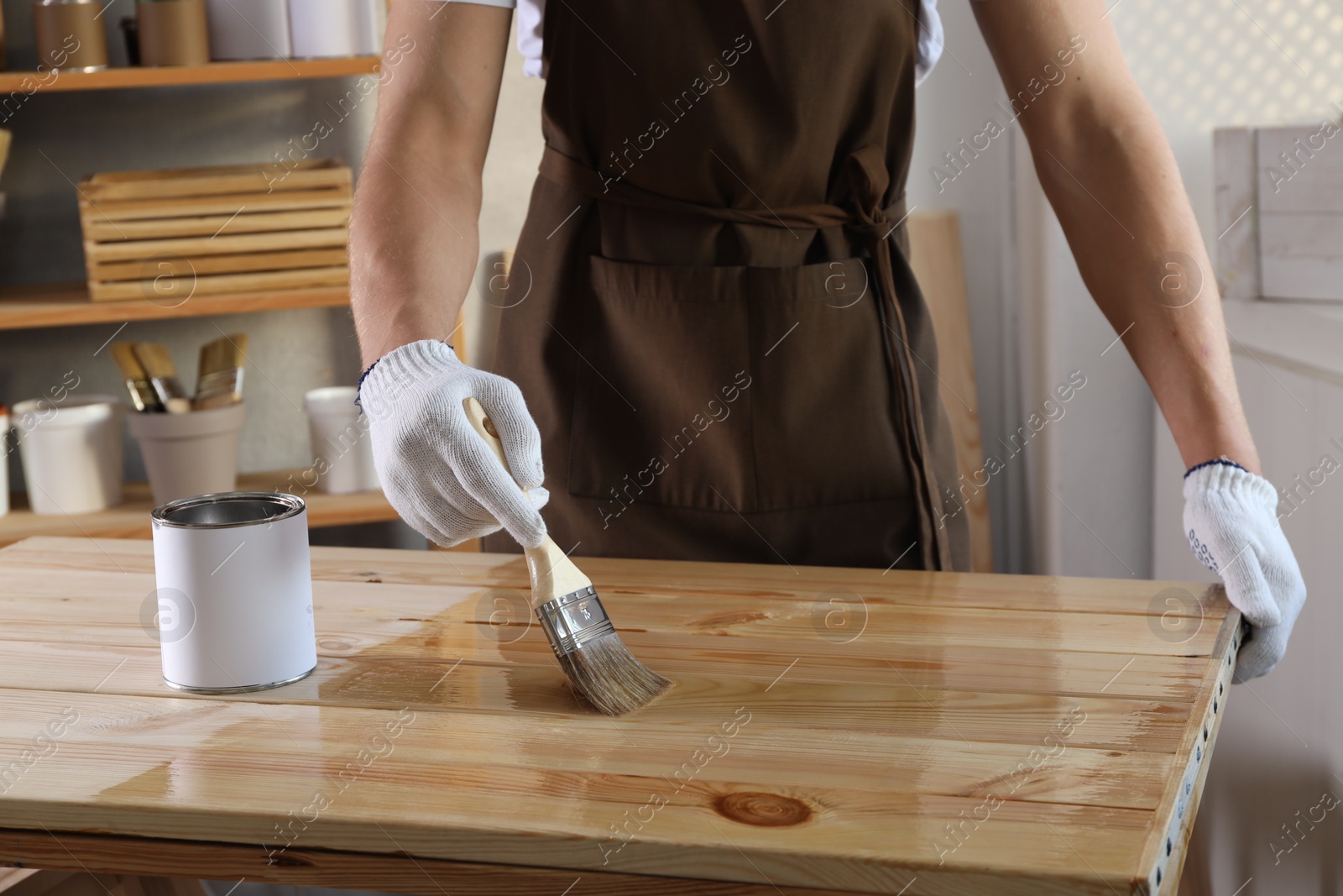 Photo of Man varnishing wooden surface with brush indoors, closeup