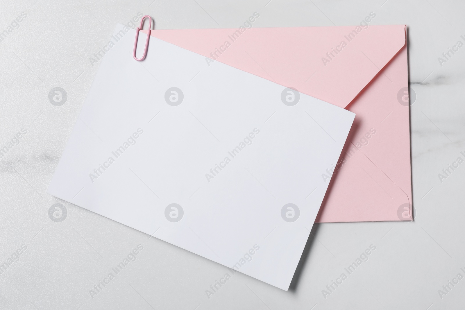 Photo of Blank sheet of paper, paperclip and letter envelope on white marble table, top view