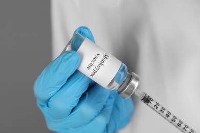 Photo of Nurse filling syringe with monkeypox vaccine from glass vial on grey background, closeup