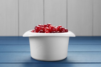 Photo of Fresh cranberries in bowl on blue wooden table, closeup