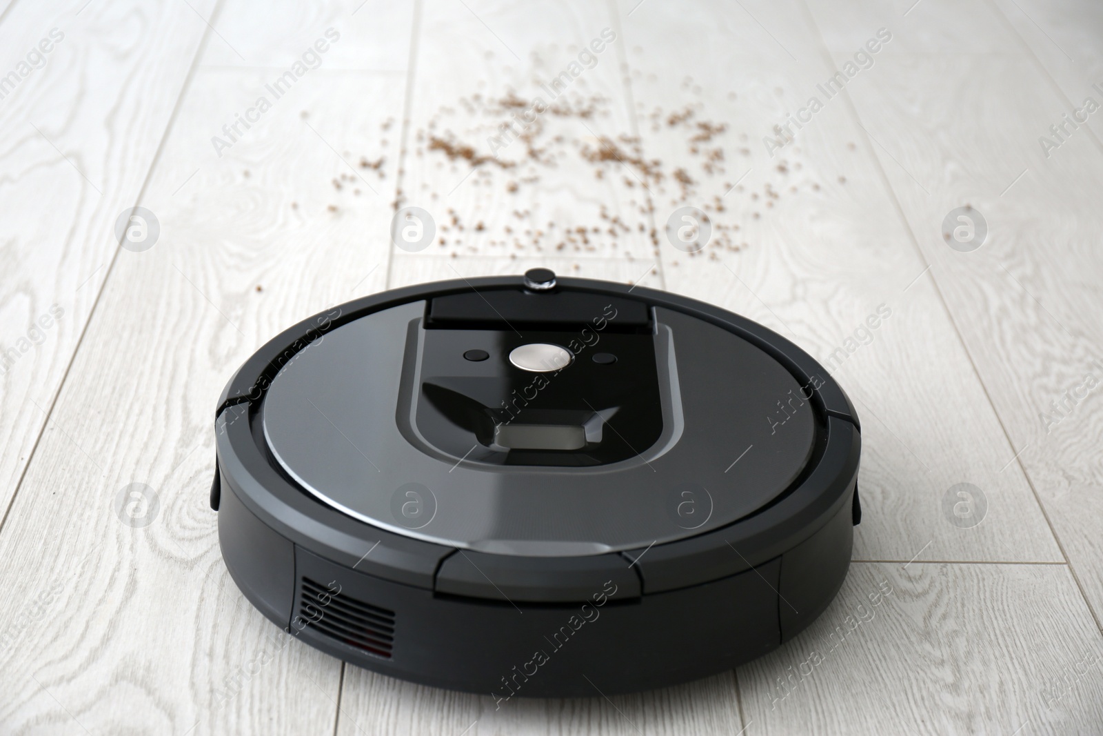 Photo of Modern robotic vacuum cleaner removing scattered buckwheat from wooden floor