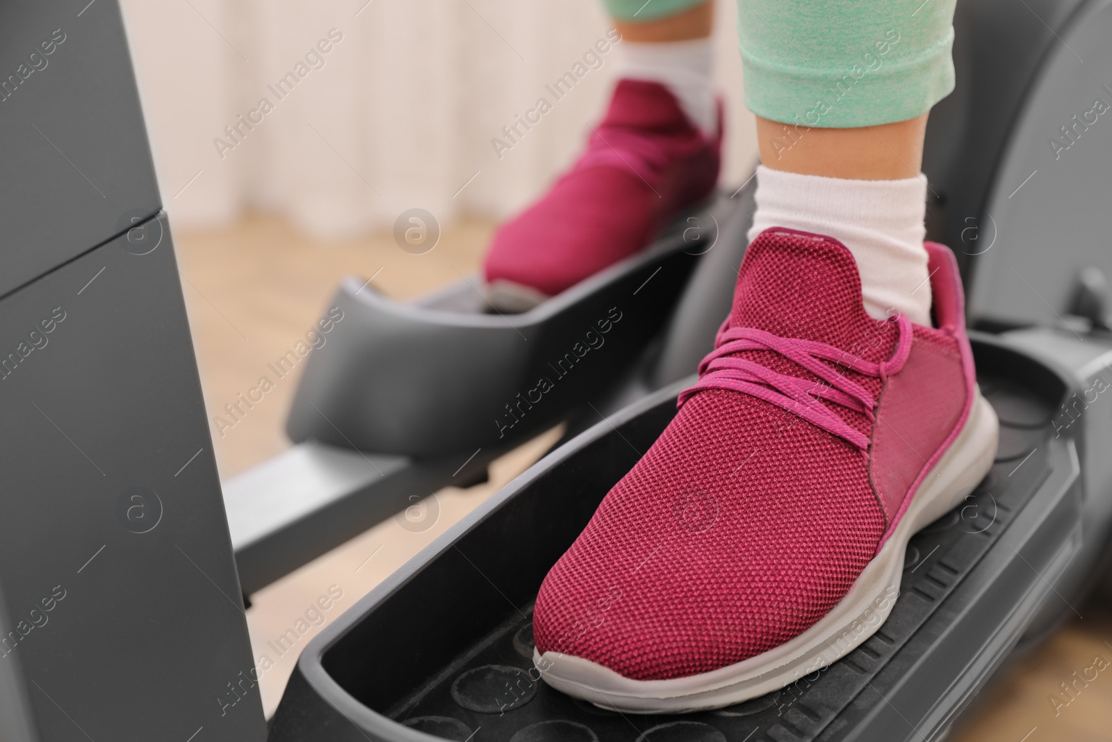 Photo of Woman using modern elliptical machine indoors, closeup