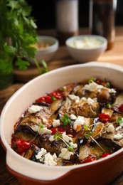 Photo of Tasty eggplant rolls with tomatoes, cheese and microgreens in baking dish on table, closeup