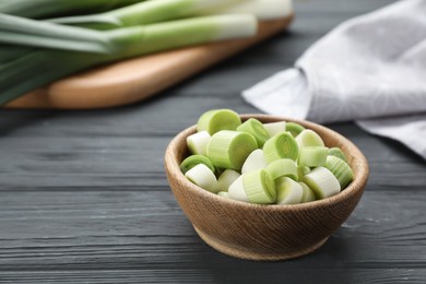 Photo of Cut fresh raw leek in bowl on grey wooden table, space for text