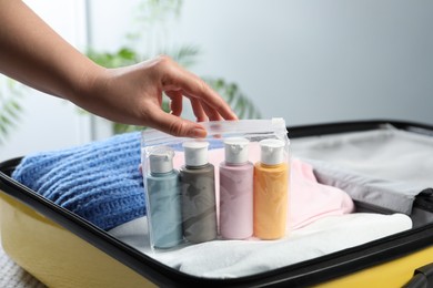 Photo of Woman with plastic bag of cosmetic travel kit packing suitcase, closeup