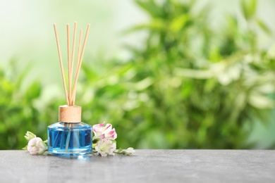 Photo of Reed air freshener and flowers on grey table against blurred green background. Space for text