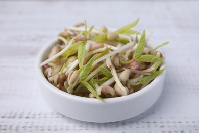 Photo of Mung bean sprouts in bowl on white wooden table, closeup