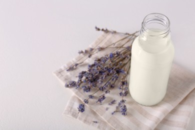 Photo of Bottle of tasty milk and lavender flowers on light table, above view. Space for text