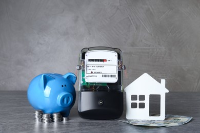Photo of Electricity meter, piggy bank, house model and dollar banknotes on grey table