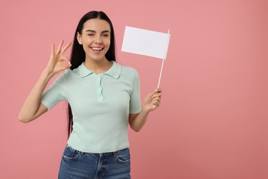 Photo of Happy young woman with blank white flag showing OK gesture on pink background. Mockup for design