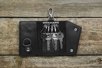 Photo of Open leather holder with keys on old wooden table, top view