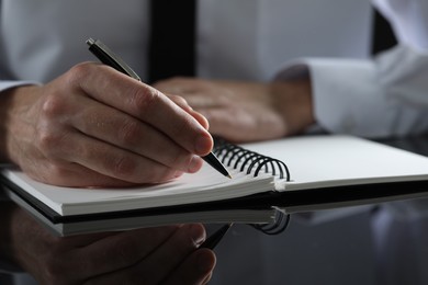 Man writing in notebook at black table, closeup