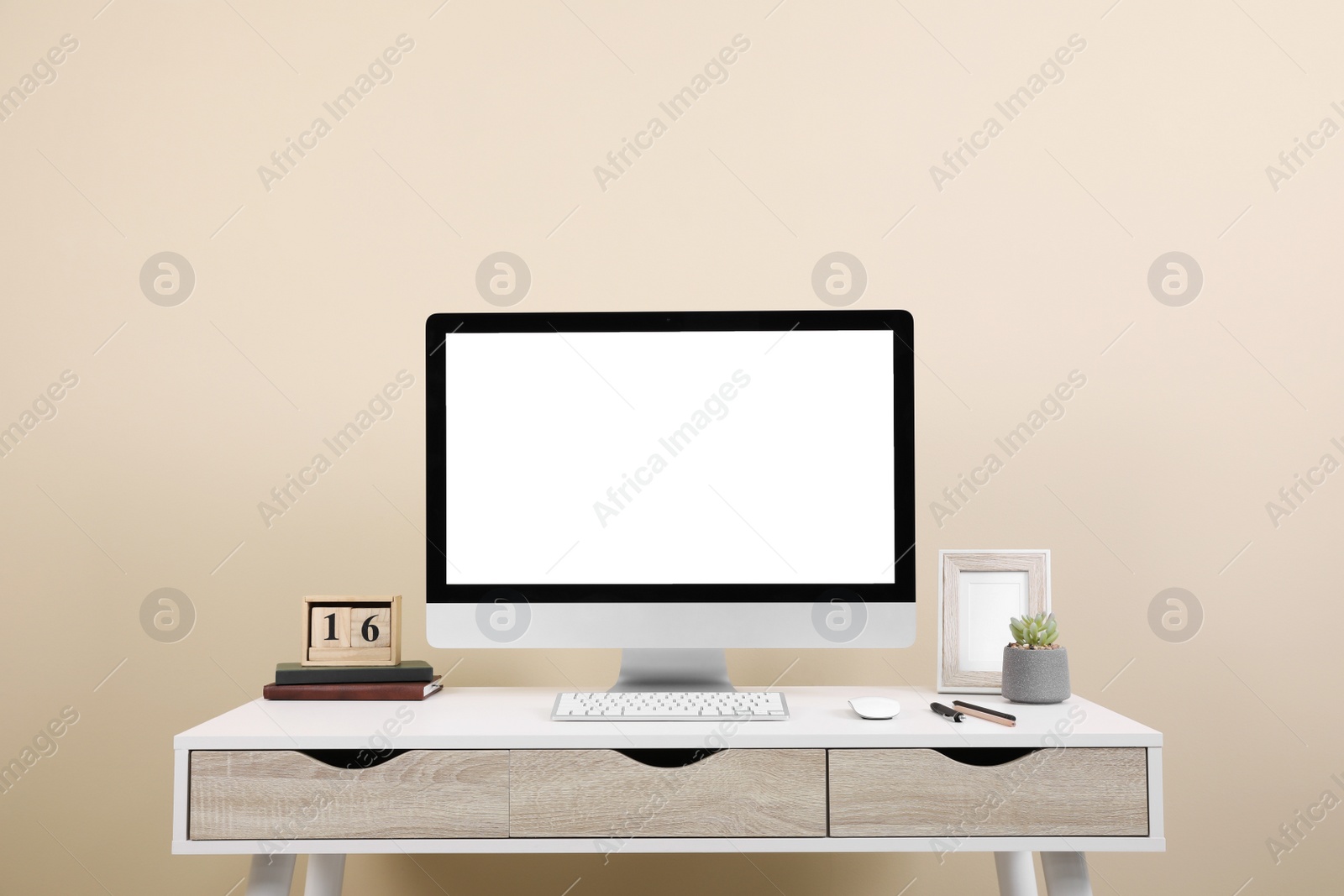 Photo of Comfortable workplace with blank computer display on desk near beige wall. Space for text