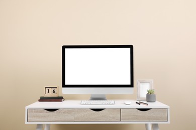 Photo of Comfortable workplace with blank computer display on desk near beige wall. Space for text