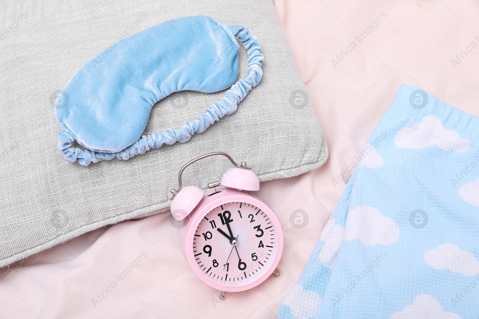 Photo of Light blue sleep mask, pillow and alarm clock on beige cloth, flat lay