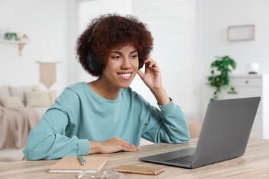 Young woman in headphones using laptop at wooden desk in room