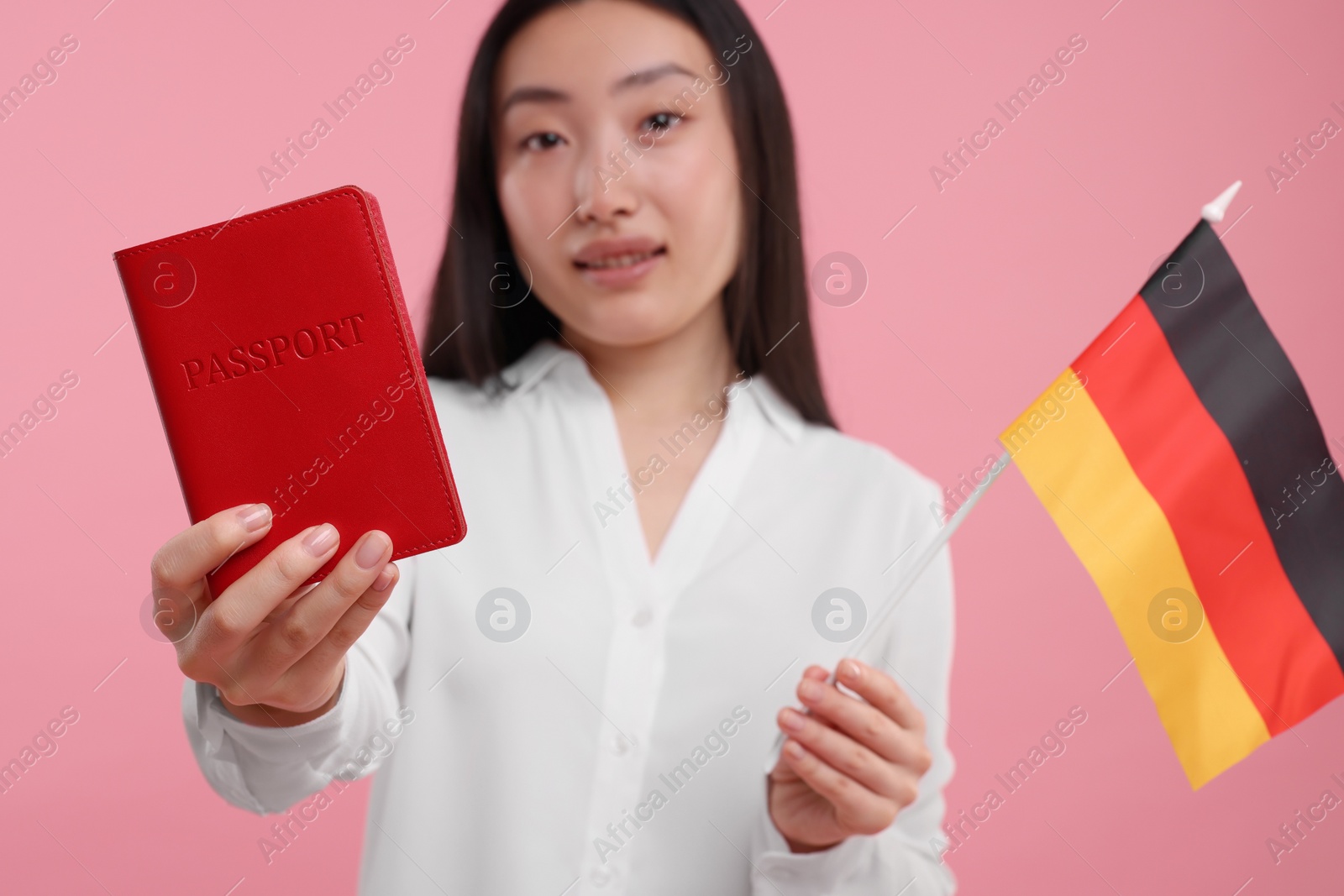 Photo of Immigration to Germany. Happy woman with passport and flag on pink background, selective focus