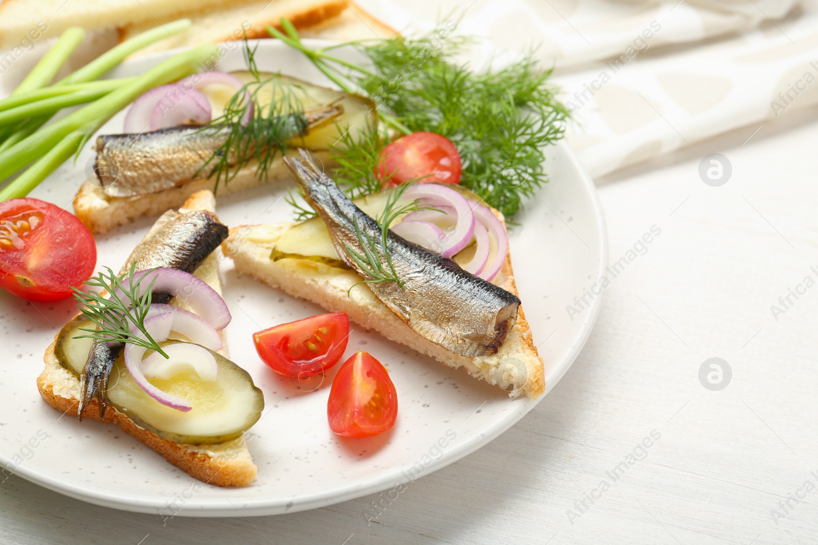 Delicious sandwiches with sprats, pickled cucumber, onion and dill served on white wooden table, closeup Photo of Delicious sandwiches with sprats, pickled cucumber, onion and dill served on white wooden table, closeup