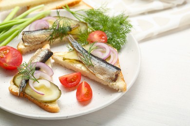 Photo of Delicious sandwiches with sprats, pickled cucumber, onion and dill served on white wooden table, closeup