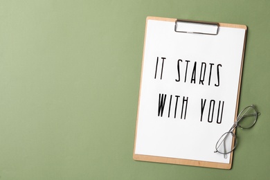 Photo of Clipboard with phrase It Starts With You and glasses on green background, flat lay. Space for text