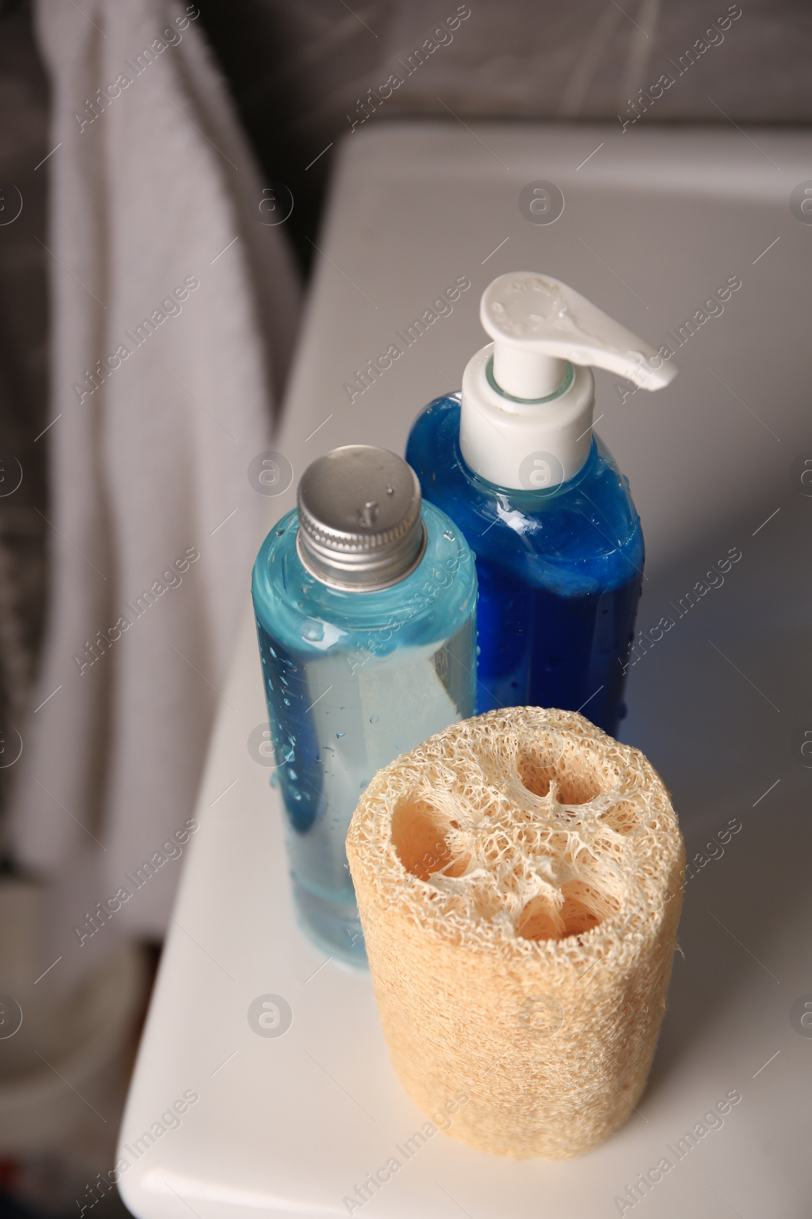 Photo of Natural loofah sponge and shower gel bottles on washbasin in bathroom