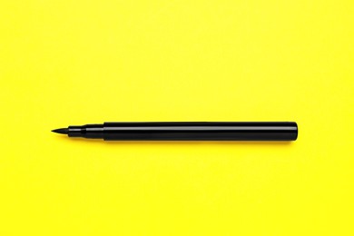 Eyeliner marker on yellow background, top view. Makeup product