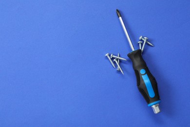 Photo of Screwdriver with black handle and screws on blue background, flat lay. Space for text