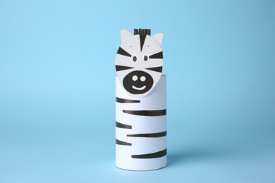 Photo of Toy zebra made from toilet paper hub on light blue background. Children's handmade ideas