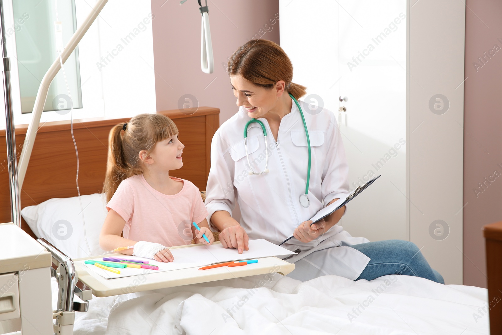 Photo of Little child with intravenous drip drawing in hospital bed during doctor's visit