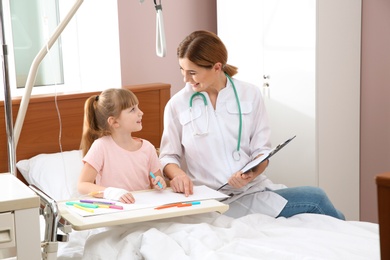 Little child with intravenous drip drawing in hospital bed during doctor's visit