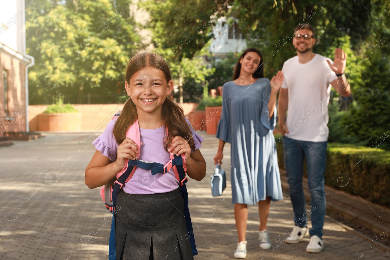 Photo of Parents waving goodbye to their daughter before school outdoors