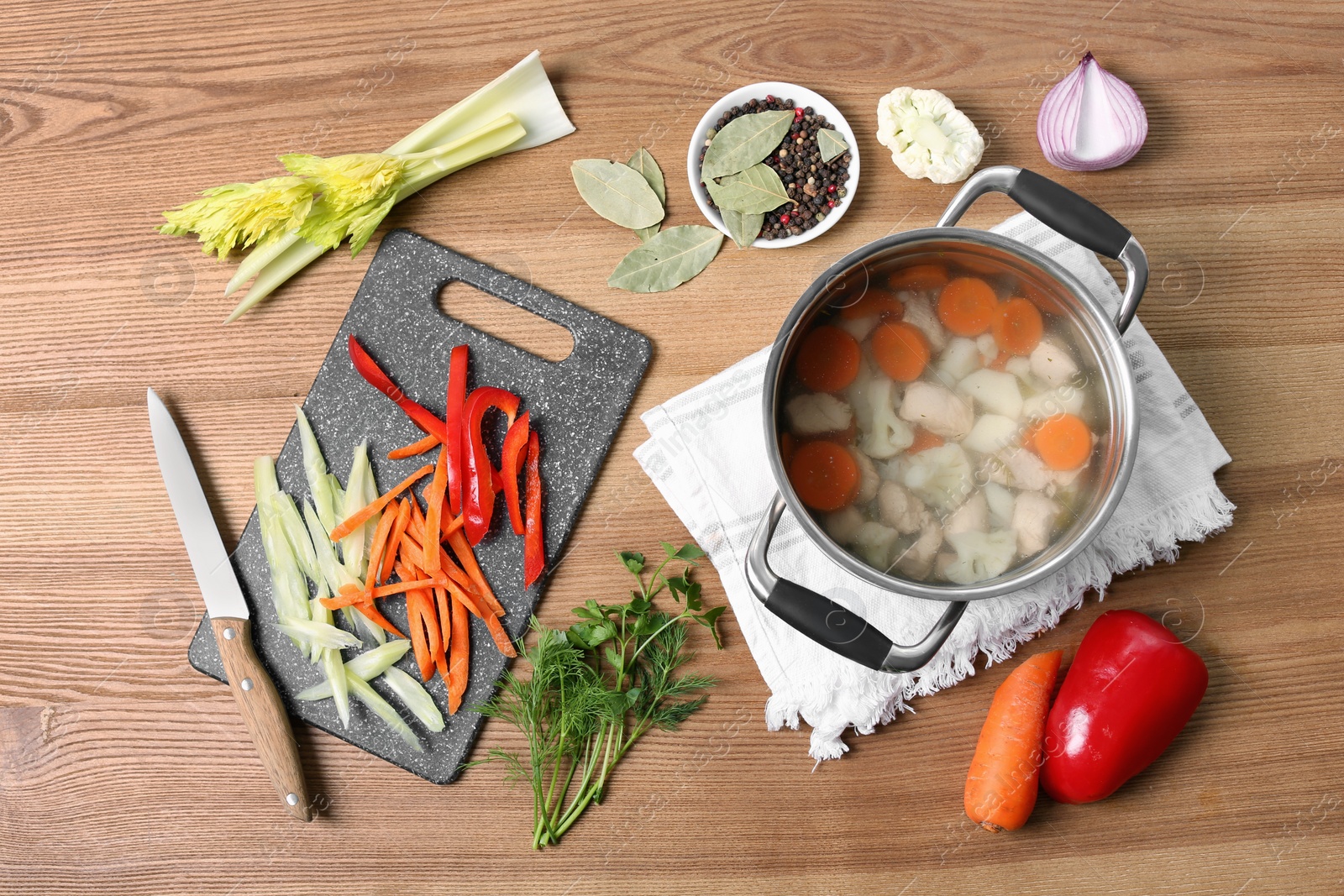 Photo of Pot of delicious vegetable bouillon and ingredients on wooden table, flat lay